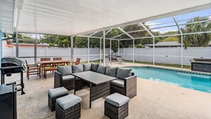 Un patio techado al aire libre con piscina, mobiliario de mimbre y una parrilla.