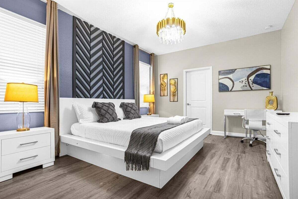 A modern bedroom with a large bed, bedside tables, a desk, and a chandelier.