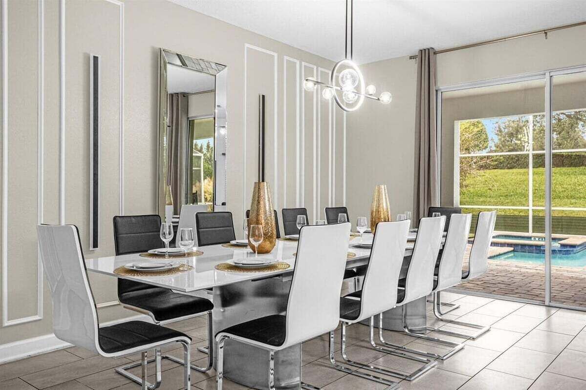 A dining room with a long table, chairs, and a large window with a view of a swimming pool.