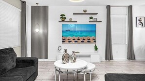 Ein modernes Wohnzimmer mit großem Fernseher, rundem Couchtisch und grauem Sofa.