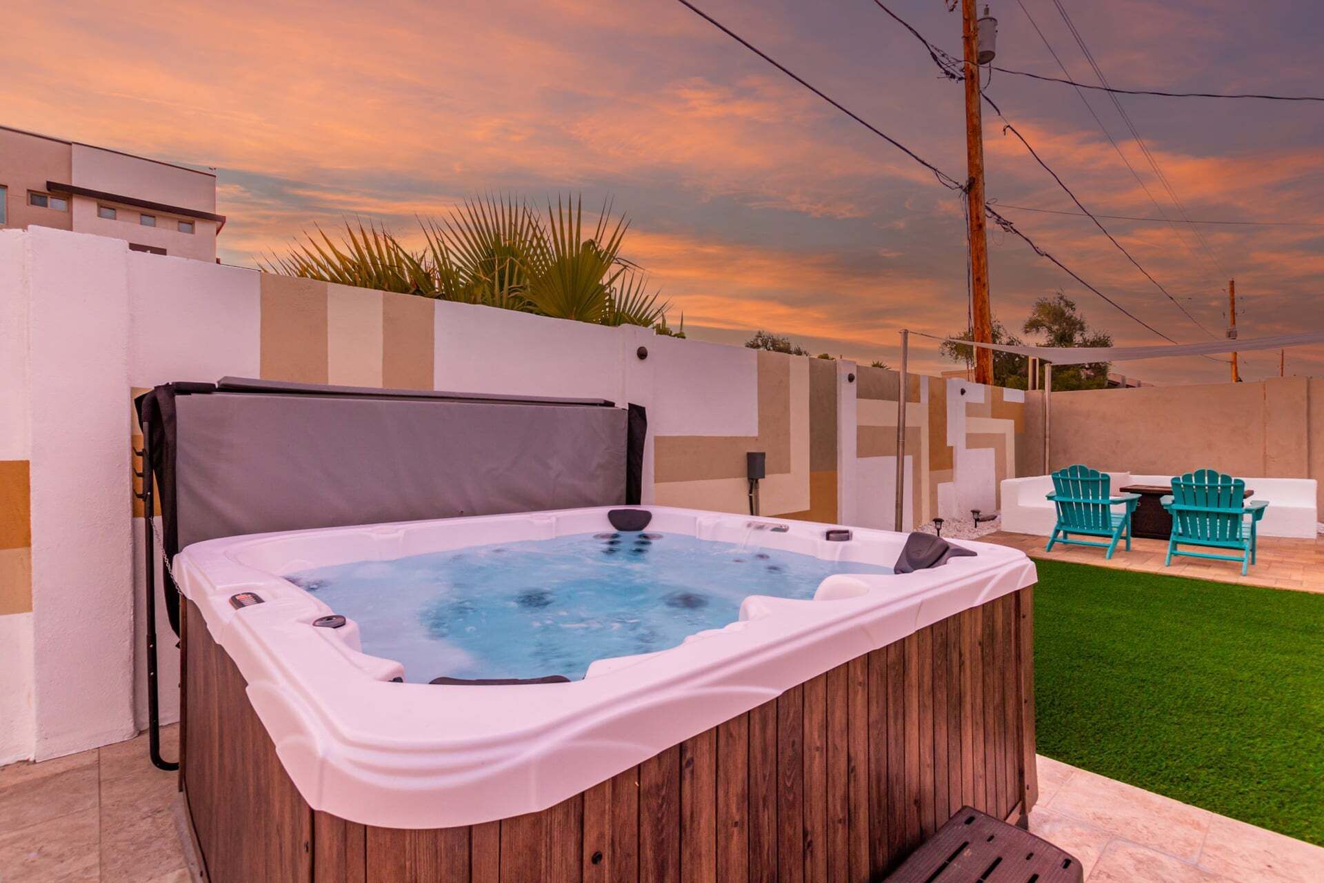 A hot tub in an outdoor setting with a sunset sky, a wooden fence, and outdoor furniture.
