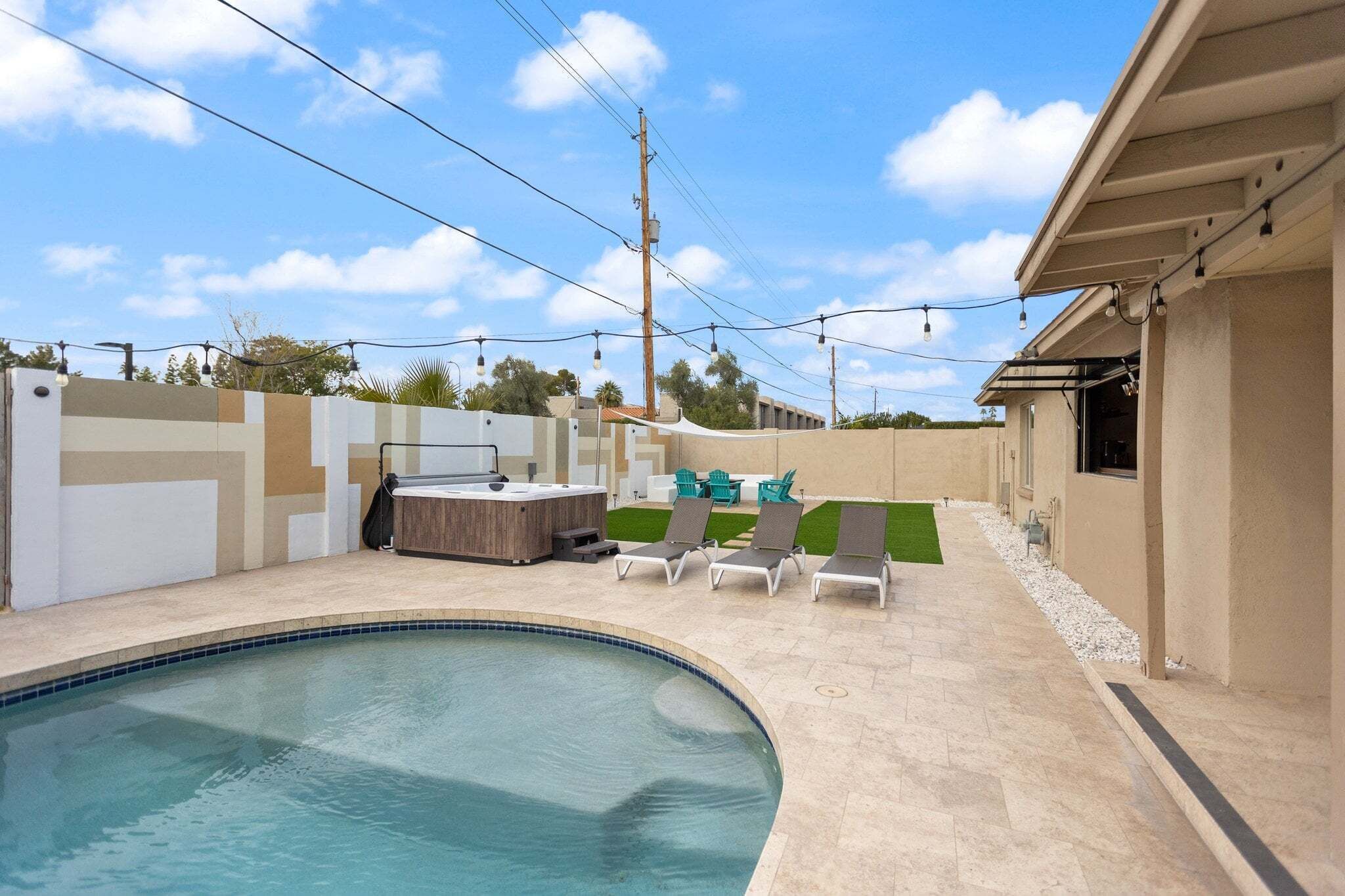 A swimming pool with lounge chairs, a hot tub, and a covered outdoor seating area.