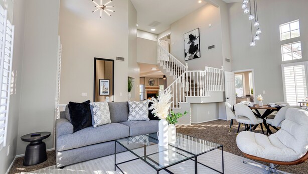 Ein geräumiges Wohnzimmer mit einem grauen Sofa, einem Glastisch, einem weißen Sessel und einer Treppe, die in eine obere Etage führt.
