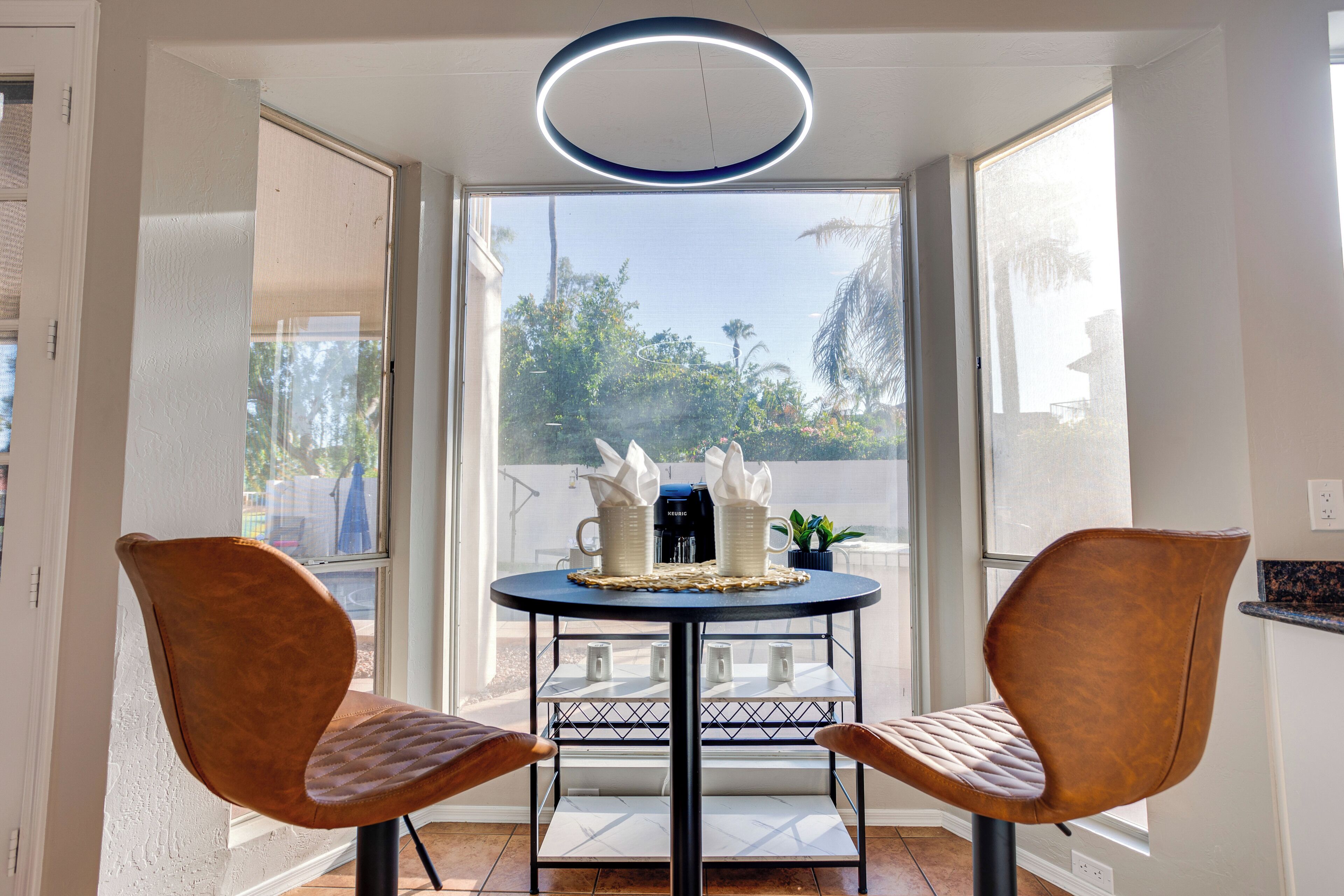 A dining area with two brown chairs, a round table, and a coffee maker.