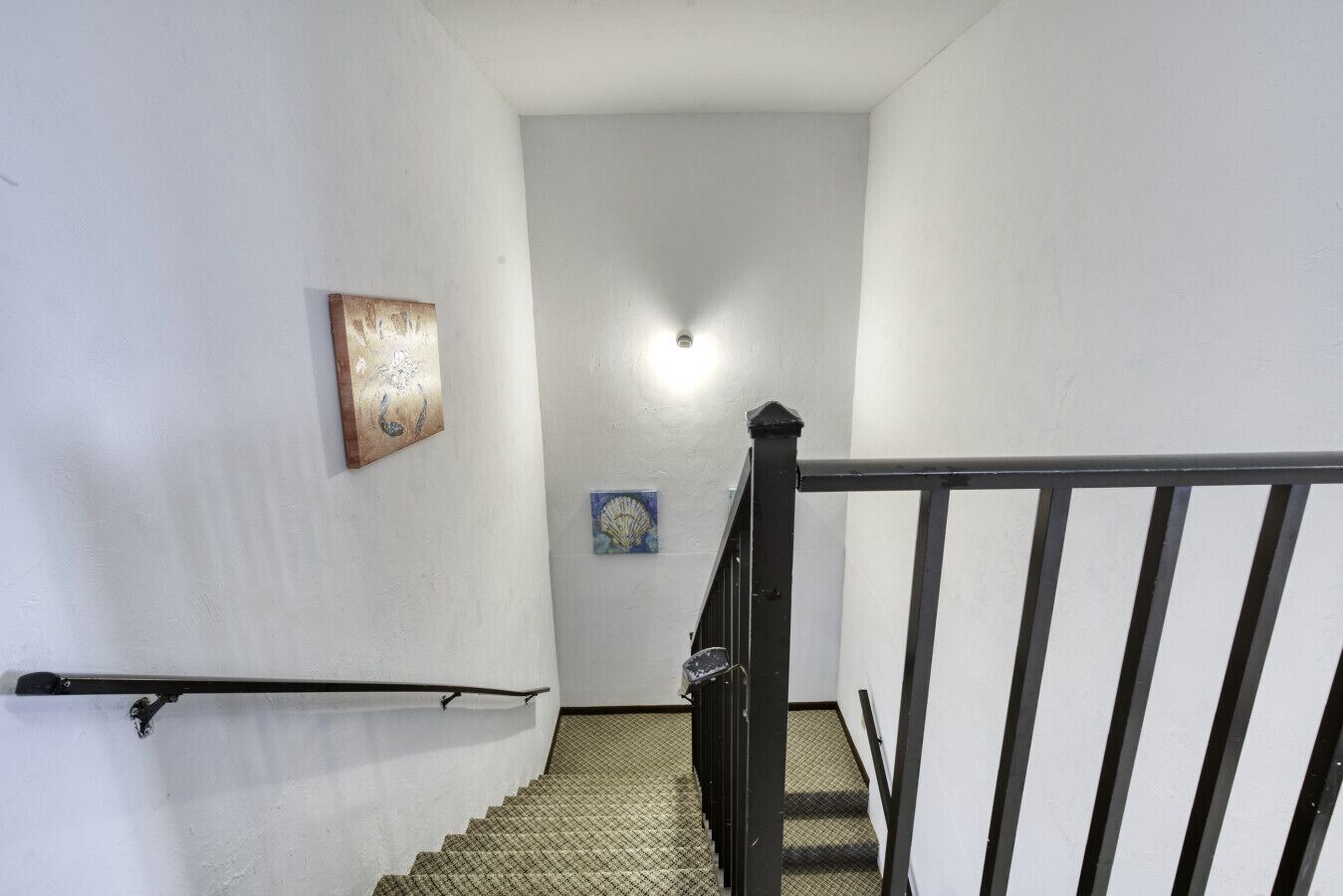A narrow stairway with a handrail, a black railing, and two wall-mounted artworks.