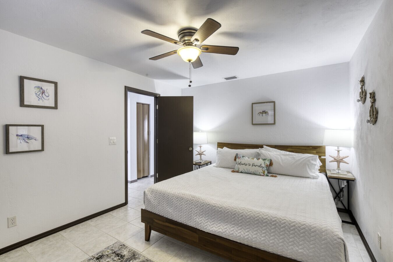 Un dormitorio con una cama, un ventilador de techo, una mesita de noche y cuadros en las paredes.