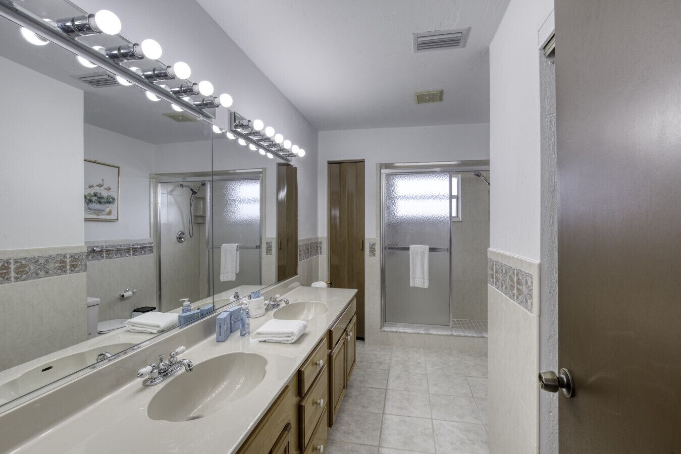 Un baño con un espejo grande, tocador con lavabo y zona de ducha.