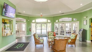 A lobby with a reception desk, wicker chairs, a television, and a view of the outside. - 8460 Crystal Cove Loop 3bed (Kissimmee)