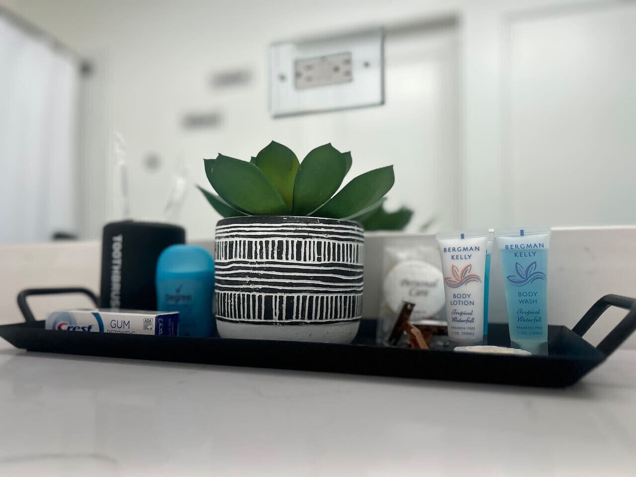 Una bandeja con una planta en maceta, un recipiente azul, una taza a rayas y dos tubos de loción corporal.