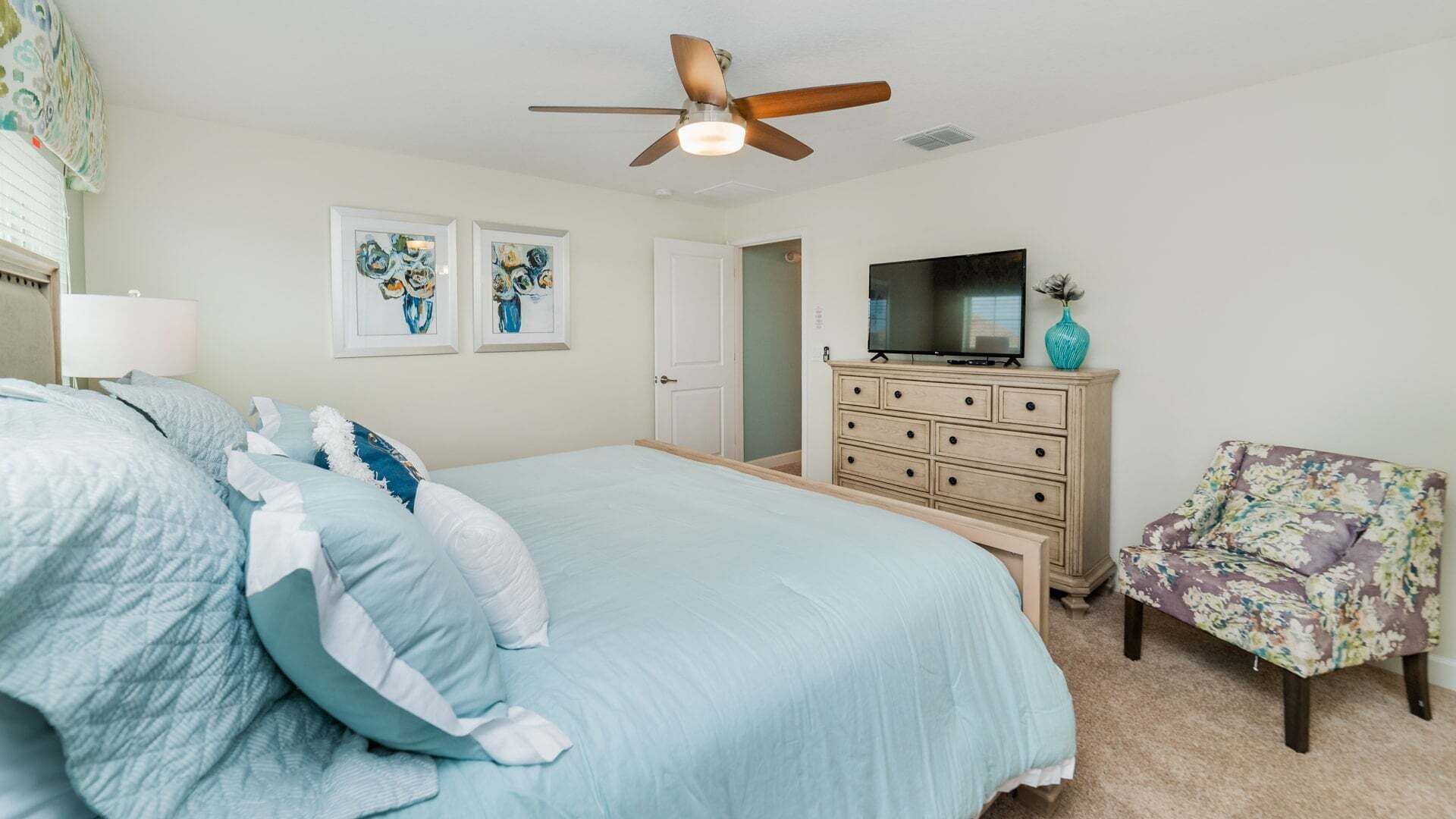 A bedroom with a bed, dresser, TV, and a chair.
