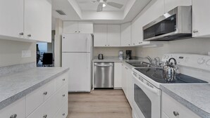 A modern kitchen with white cabinets, a stainless steel refrigerator, a microwave, a kettle, and a dishwasher. - Anc903 (Siesta Key)
