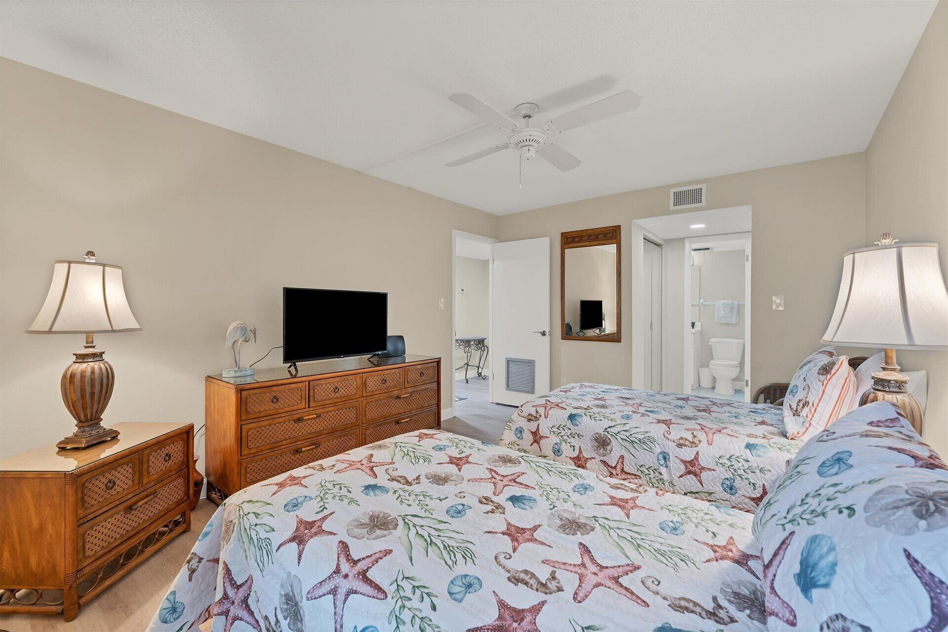 Ein Schlafzimmer mit Bett, Kommode, Fernseher, Deckenventilator und einer Badezimmertür.