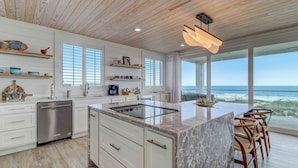 Una cucina moderna con mobili bianchi, una grande isola e vista sull'oceano.