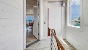 Un corridoio con pannelli bianchi, soffitto in legno e vista su una sala da pranzo con tavolo e sedie.