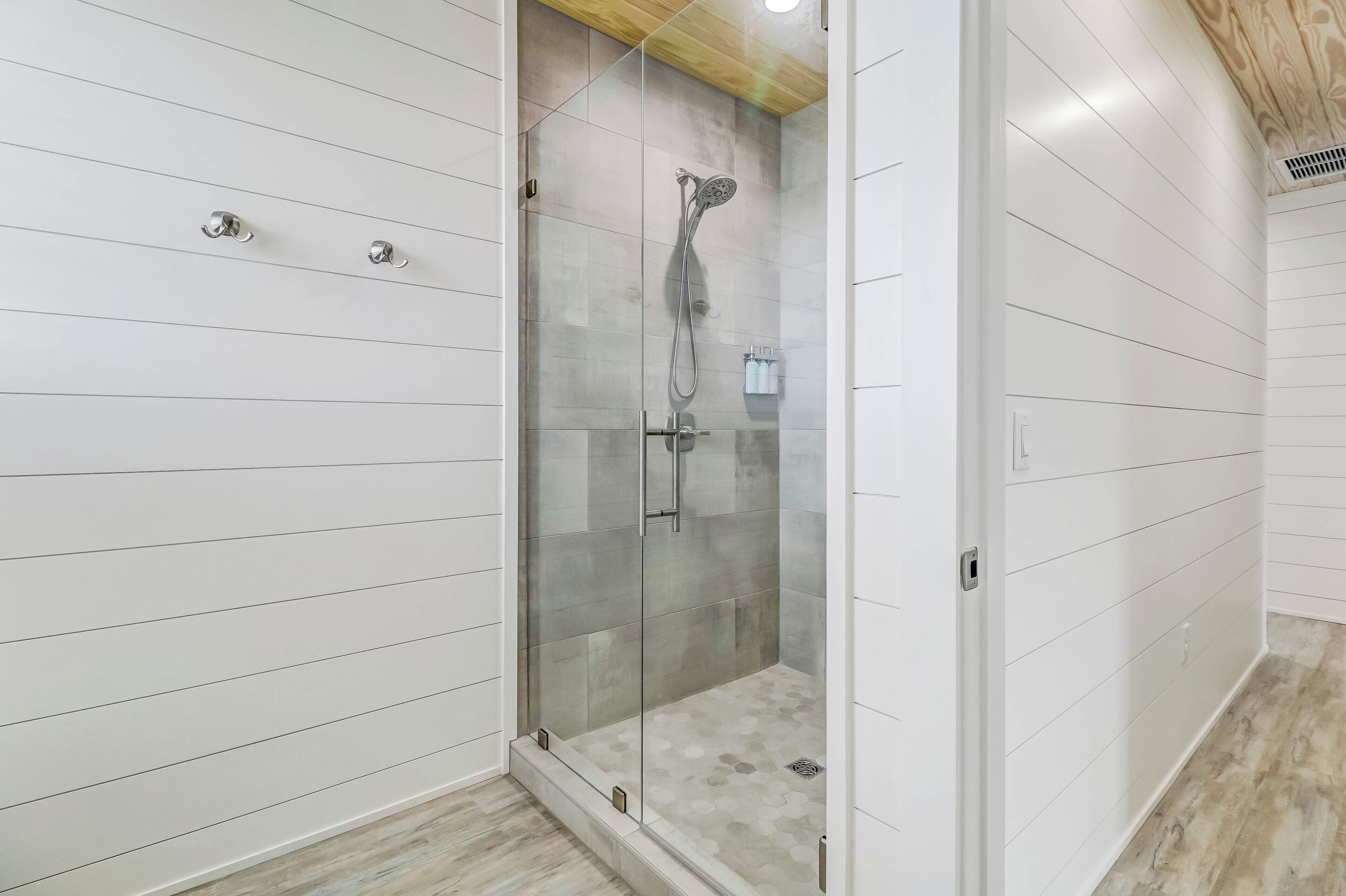 A modern bathroom with a glass-enclosed shower, white tiled walls, and a wooden ceiling.