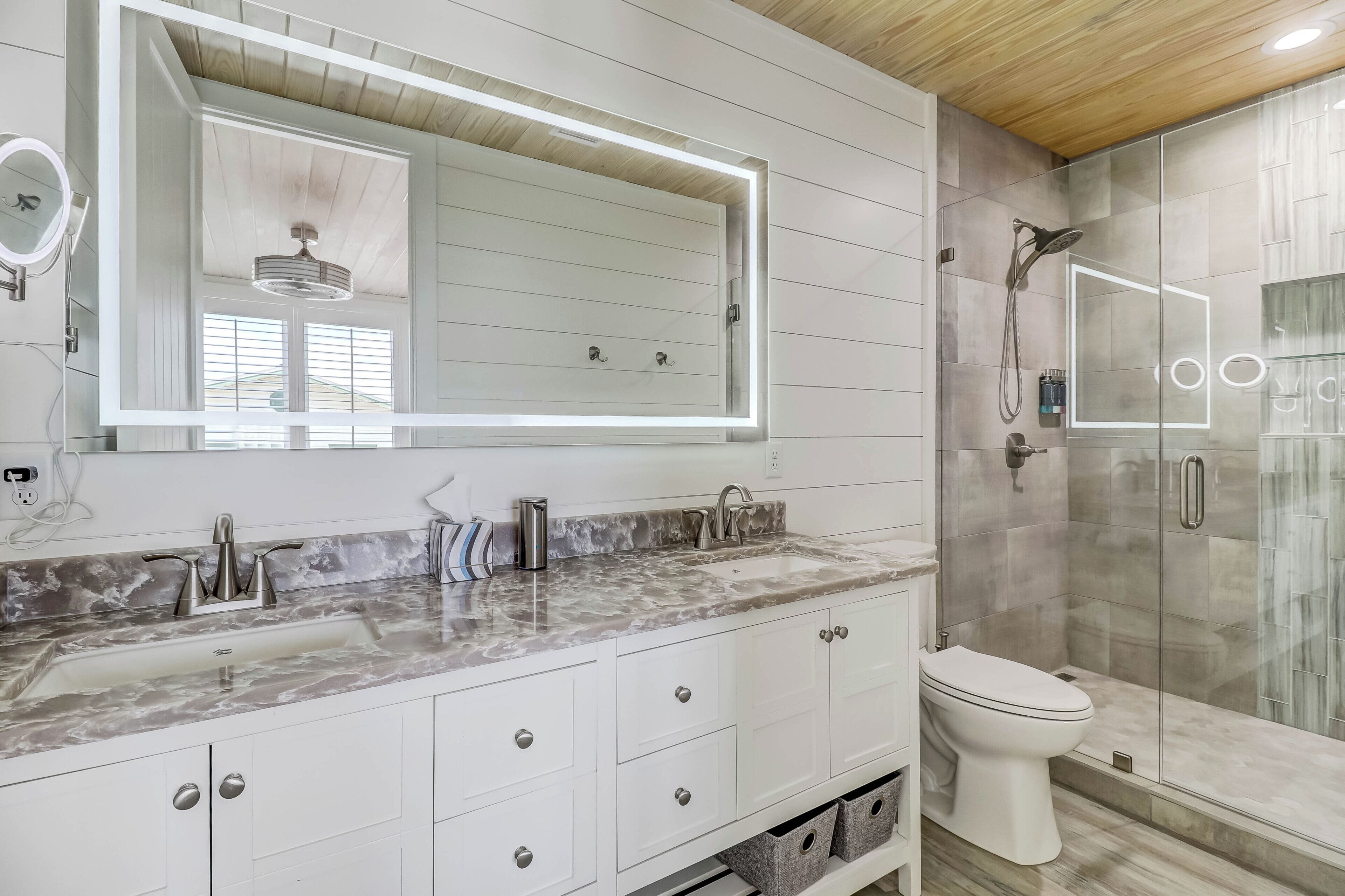 A modern bathroom with a marble vanity, a large mirror, a shower enclosure, and a toilet.