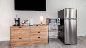 Pieni keittiönurkkaus, jossa on mikroaaltouuni, jääkaappi, puinen kaappi ja seinälle asennettu taulutelevisio.