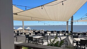Een buitenruimte met tafels en stoelen, een houten terras en uitzicht op de oceaan.