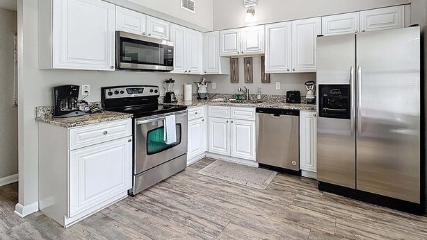A kitchen with white cabinets, stainless steel appliances, a microwave, oven, dishwasher, and granite countertops. - 3517 River Grove Drive (Tampa)