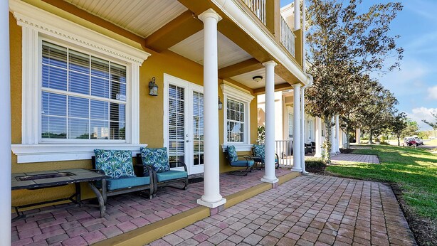 A covered porch with outdoor seating, a brick pathway, and a tree-lined street. - 7407 Excitement DR (Kissimmee)