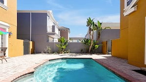 A swimming pool with a brick border, surrounded by a patio area with plants and a chair. - 7407 Excitement DR (Kissimmee)