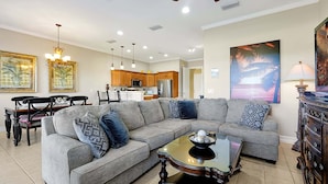 A modern living room with a sectional sofa, a glass coffee table, and a dining area with a wooden table and chairs. - 7407 Excitement DR (Kissimmee)