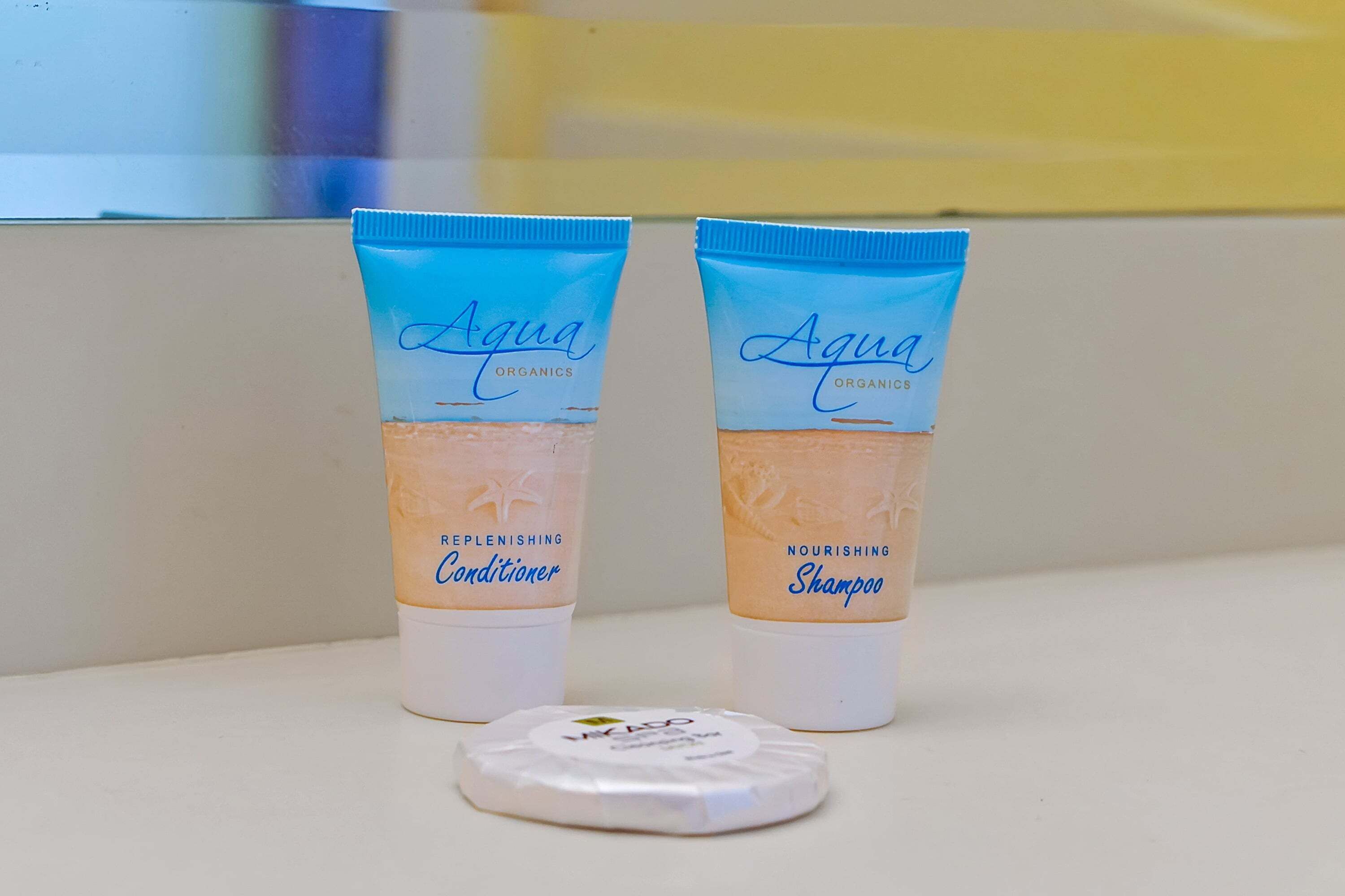 Deux tubes de shampoing et d’après-shampoing de la marque Aqua Organics sont posés sur une surface blanche, avec un bouchon blanc devant.