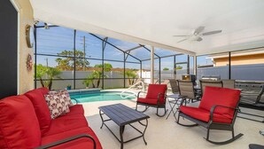 Ein Außenbereich mit Terrasse, Pool, roter Sitzgelegenheit, Tisch und Grill.