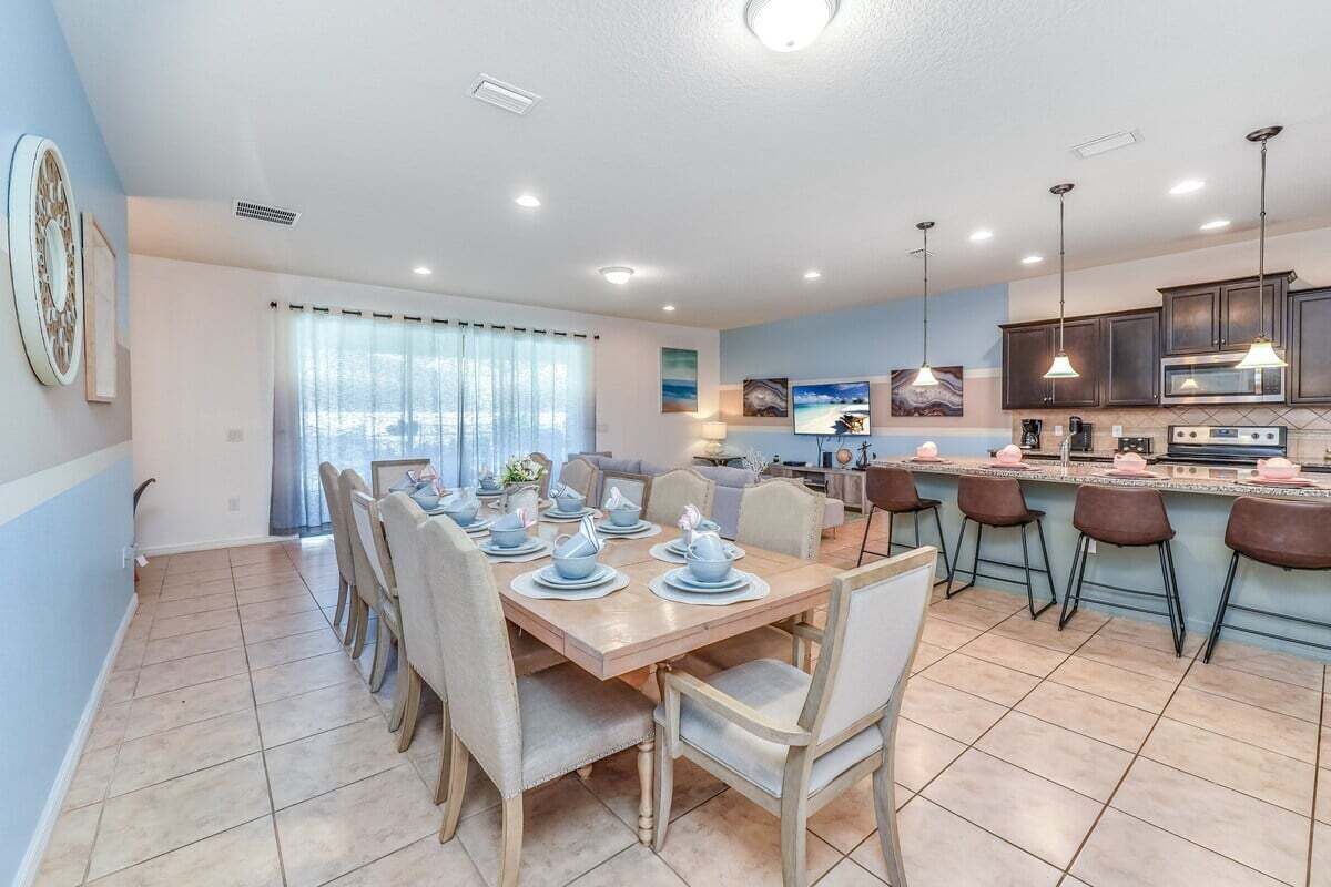 Een moderne keuken met een eethoek, met een grote tafel voor zes personen, barstoelen en een keukeneiland met een magnetron en fornuis.