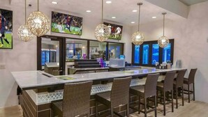 A modern bar area with a long counter, wicker chairs, and decorative hanging lights. - 8872ql-backup · Newly Furnished 9BR Villa With Pool/spa (Kissimmee)