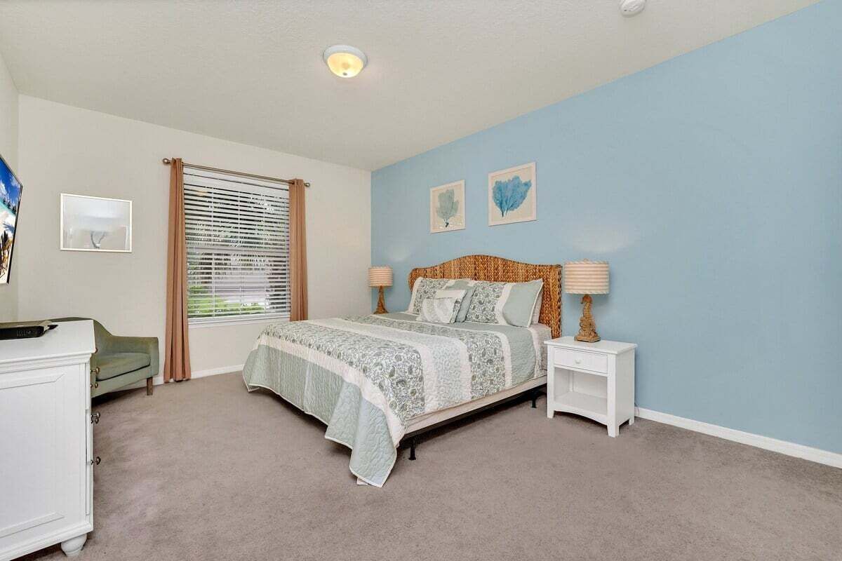 Une chambre à coucher comprenant un lit, des tables de chevet, une commode et une fenêtre avec des stores.