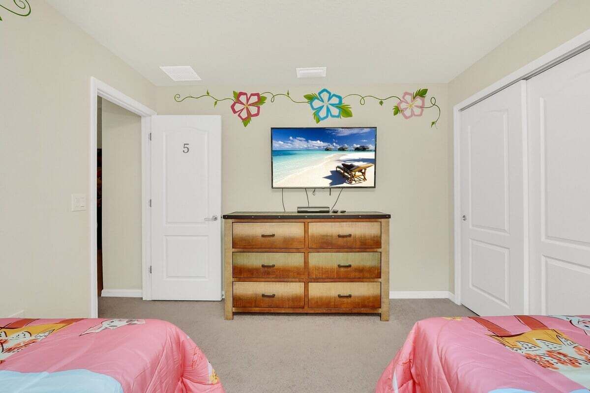 A bedroom with two beds, a dresser, a TV on the wall, and a door marked with the number 5.