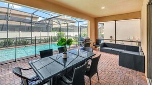 A glass-enclosed patio with a pool, outdoor furniture, and a grill. - 8872ql-backup · Newly Furnished 9BR Villa With Pool/spa (Kissimmee)