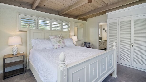 A bedroom with a white bed, wooden headboard, and a ceiling fan.