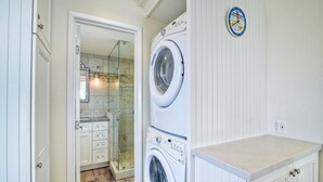 A laundry room with two stacked washing machines, a glass shower enclosure, and a white countertop.