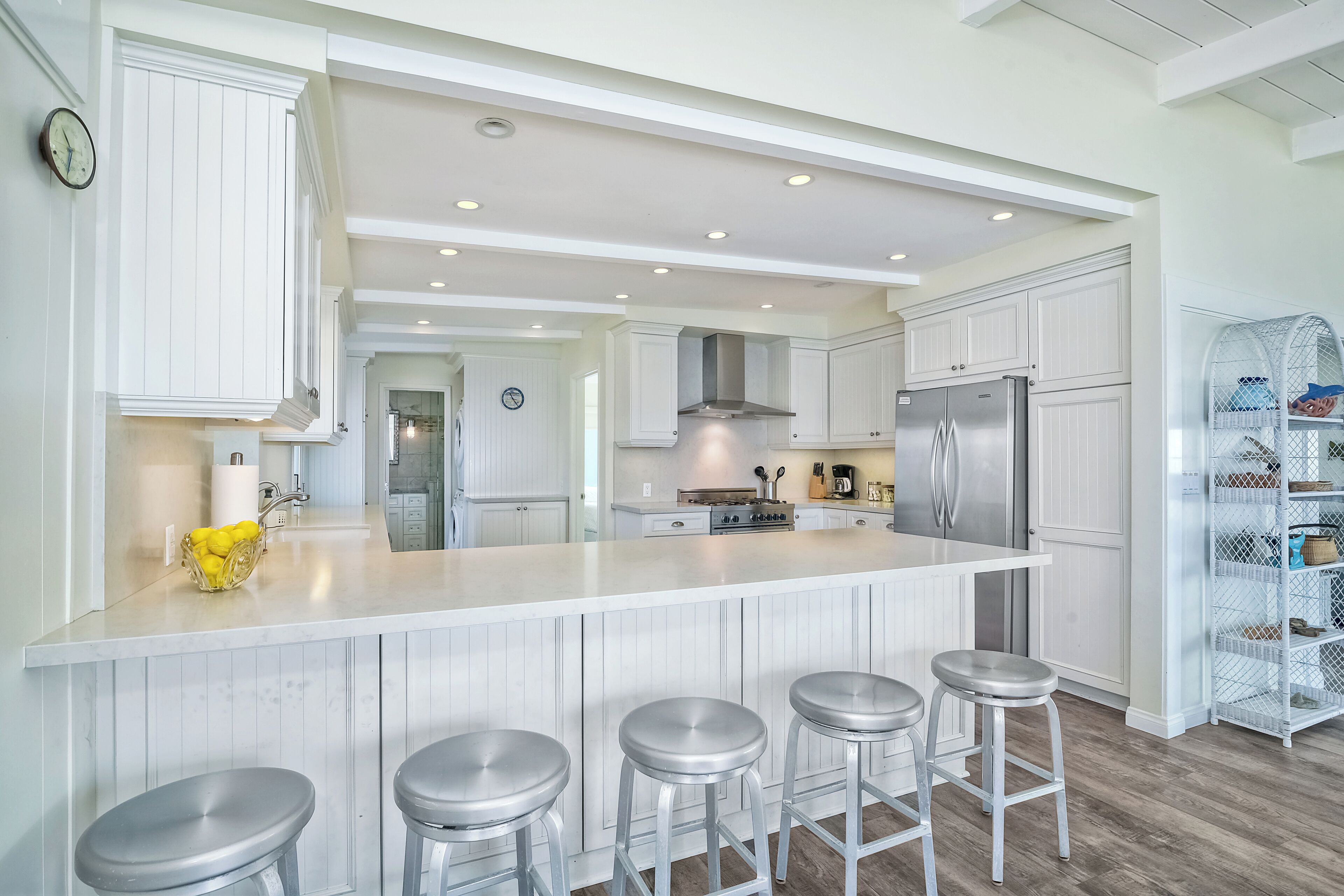 A modern kitchen with white cabinetry, a central island with stools, stainless steel appliances, and a built-in pantry.