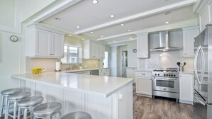 A spacious kitchen with white cabinetry, a large island with bar stools, stainless steel appliances, and recessed ceiling lighting.