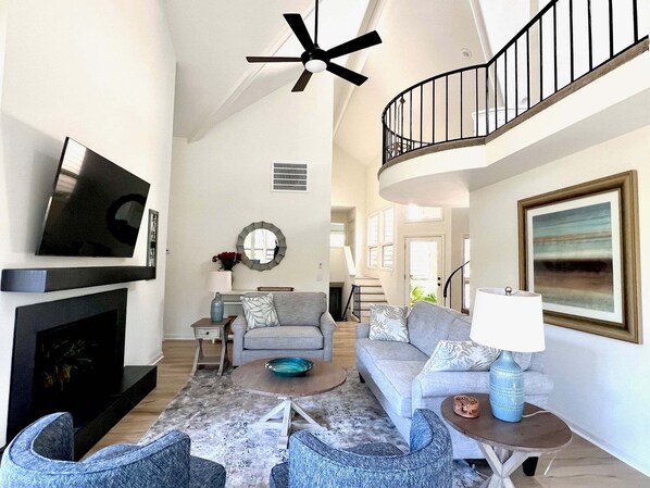 A spacious living area with a fireplace, a television, a ceiling fan, a staircase, and a large painting. - 2975 Deer Point Dr (Seabrook Island)