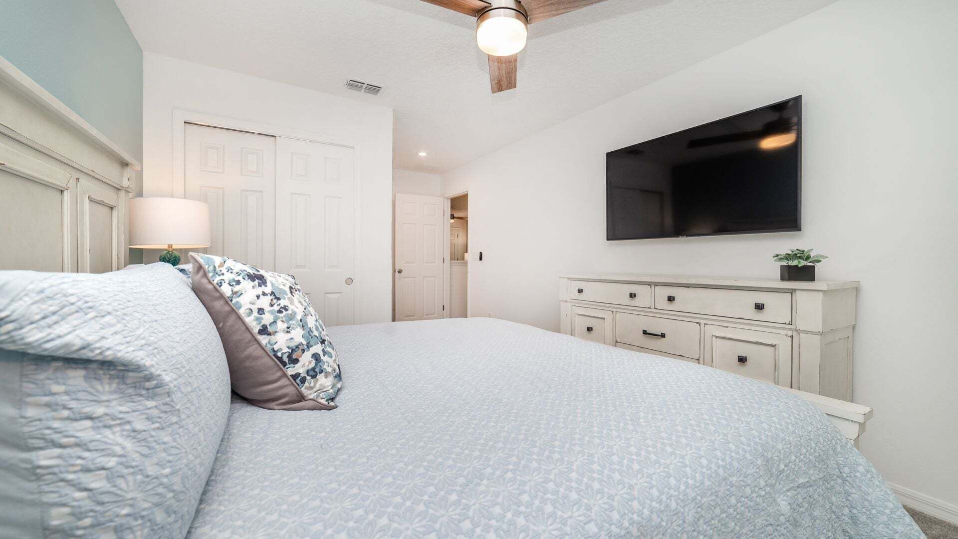A bedroom with a bed, a dresser, a TV, and a ceiling fan.