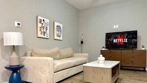 A living room with a beige sofa, a blue side table, a wooden coffee table, a TV displaying the Netflix logo, and a wooden cabinet. - A+ for Workers/family,bychoctaw,longstaydiscount (Durant)