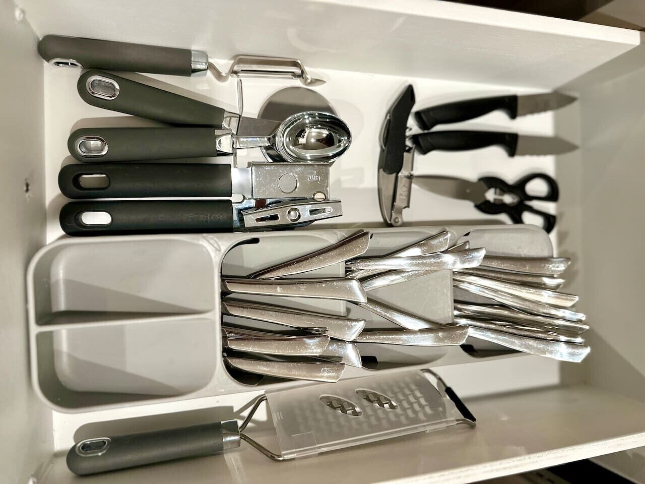 A drawer containing various kitchen utensils including spatulas, a grater, and a can opener.