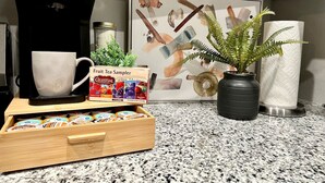 A kitchen counter with a coffee maker, a mug, a box of tea samples, a potted plant, and a framed artwork. - A+ for Workers/family,bychoctaw,longstaydiscount (Durant)