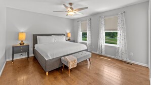 A bedroom with a bed, bedside tables, a bench, a ceiling fan, and windows with curtains. - 3229 Eads Ave (St. Louis)