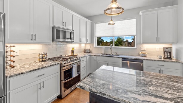A modern kitchen with white cabinets, a granite countertop, stainless steel appliances, and a pendant light. - 3229 Eads Ave (St. Louis)