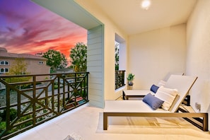 A balcony with a view of a sunset, a white cushioned lounge chair, and a small table with a plant. - 343 Oak Avenue (Carlsbad)