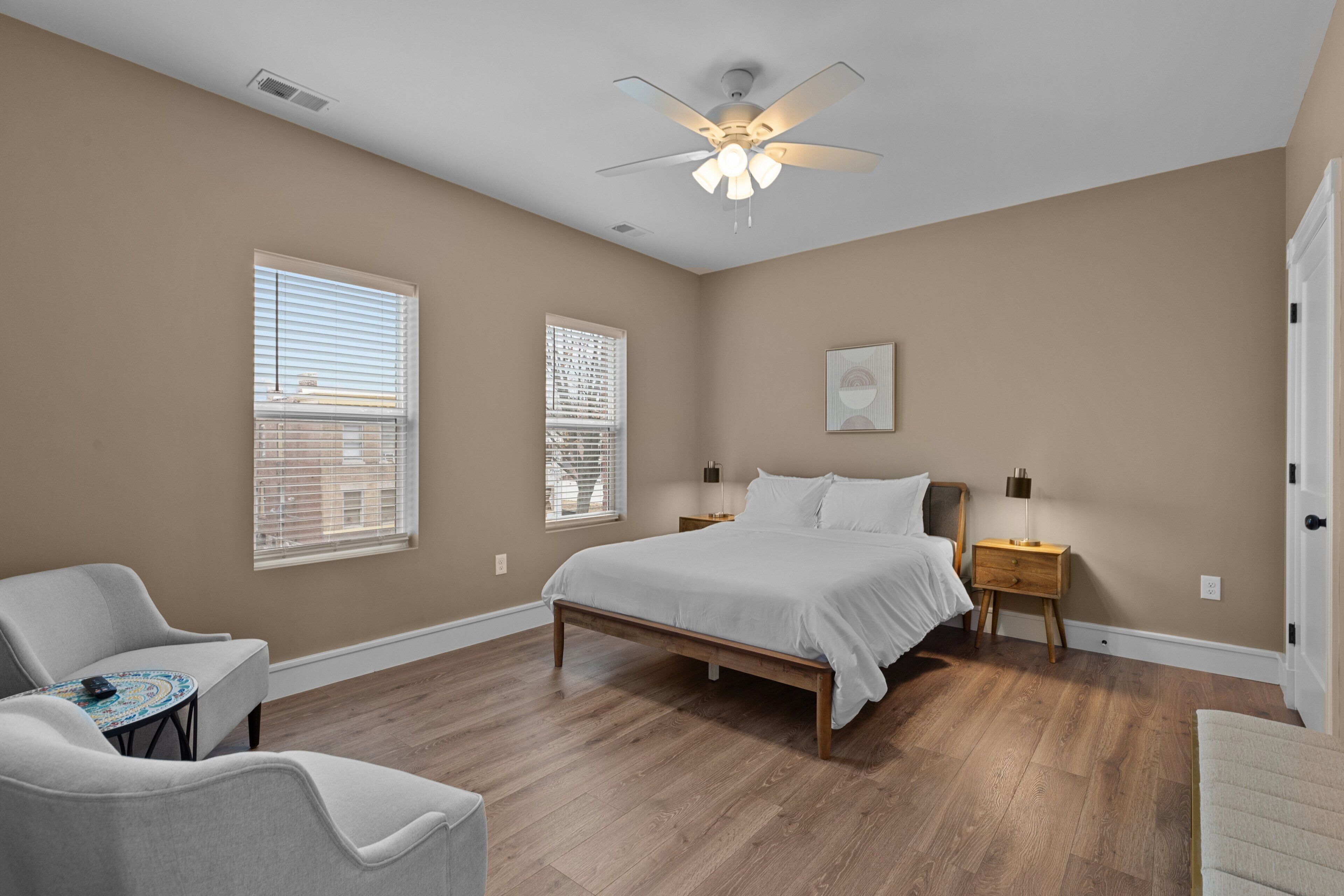 A bedroom with a bed, two bedside tables, a chair, and a ceiling fan.