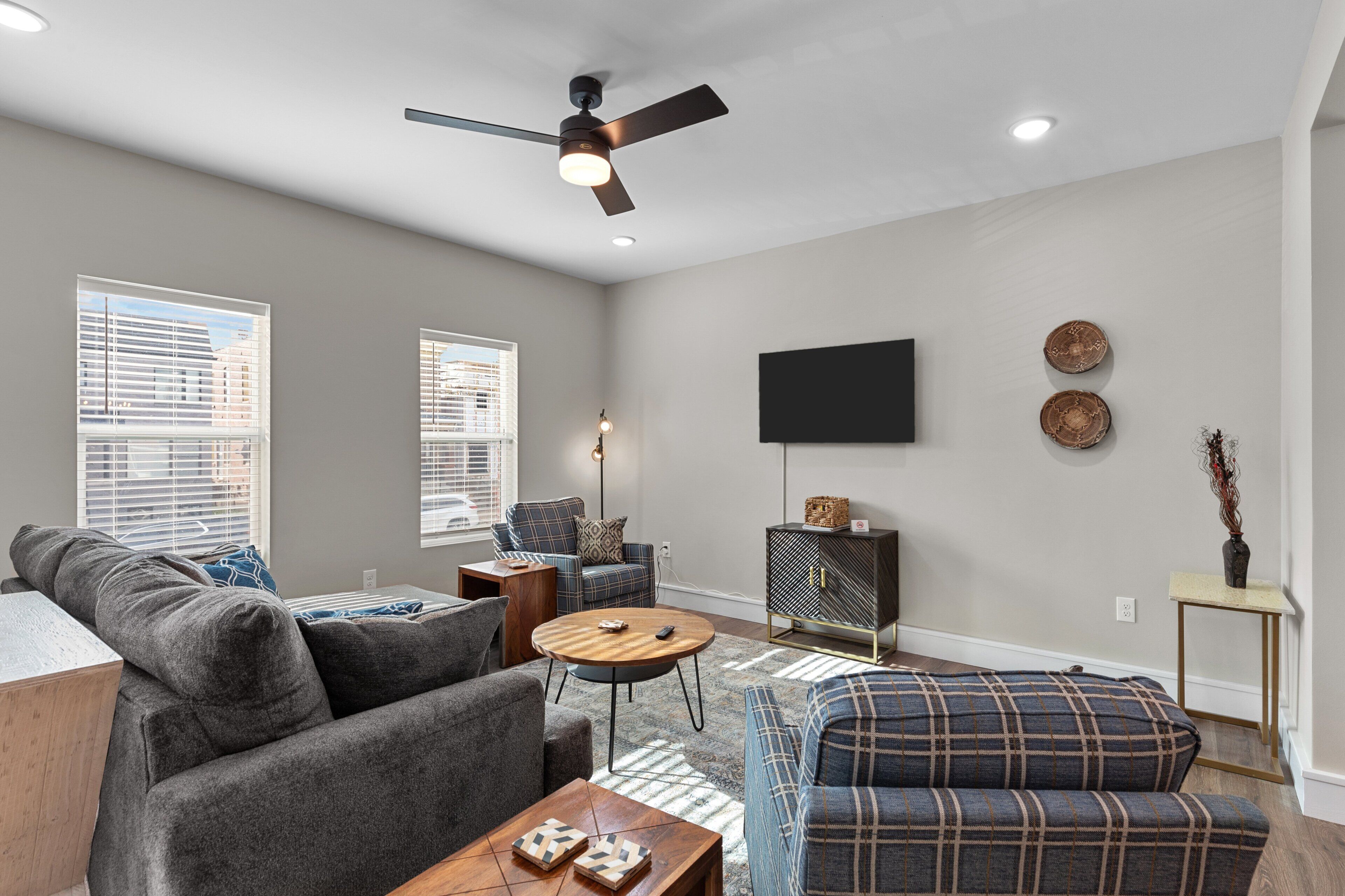 Un salon moderne avec un canapé gris, un canapé à carreaux bleus, une table basse en bois et un ventilateur de plafond.