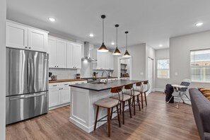 Una cocina moderna con armarios blancos, electrodomésticos de acero inoxidable y una isla central con taburetes de bar.