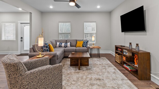 A modern living room with a sectional sofa, patterned armchairs, a coffee table, a wooden console table with decorative items, and a flat-screen TV mounted on the wall. - 3323: Uptown Elegant Escape by JZ Vacation Rentals (St. Louis)