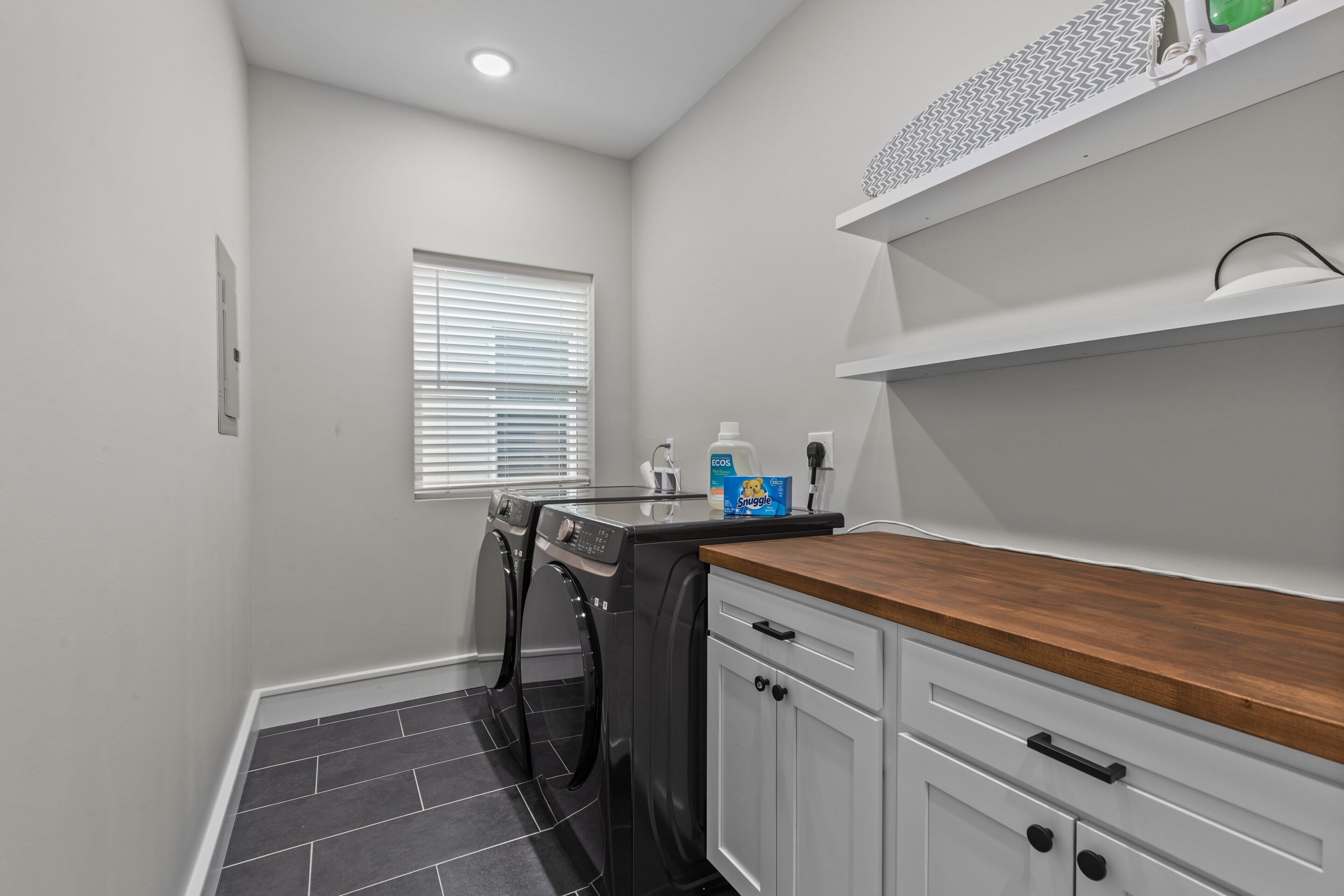 A laundry room with a washing machine, dryer, and a wooden countertop with a shelf above.